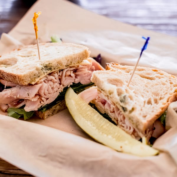 Smoked turkey sandwich on rustic bread with lettuce and a pickle spear, served on brown paper.