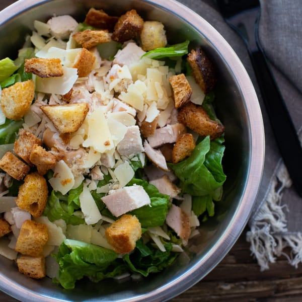 Caesar salad with chicken, croutons, and parmesan cheese in a metal bowl.
