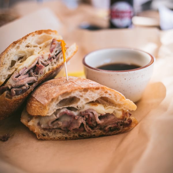 A sliced BBQ brisket sandwich with melted cheese and a side of au jus on parchment paper.