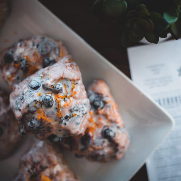 Close-up of blueberry fritters with white glaze and orange zest on a white rectangular plate.