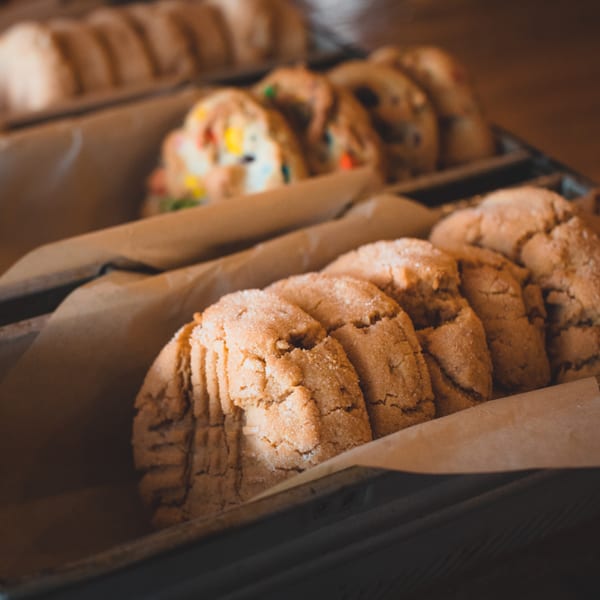 Close-up of freshly baked sugar cookies and M&M cookies in metal trays lined with parchment paper.