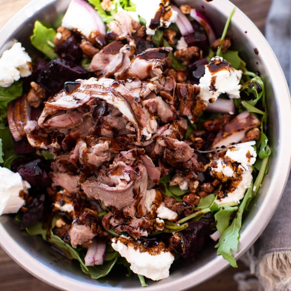 Close-up of a BBQ brisket salad with goat cheese, beets, and balsamic glaze in a metal bowl.