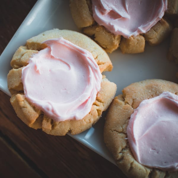 Close-up of several sugar cookies with pink frosting on a white plate, on a wooden table.