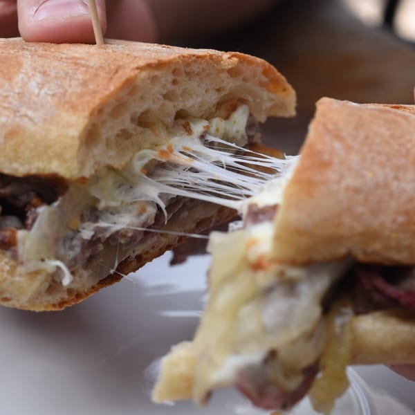 A person pulling apart a cheesy BBQ sandwich, showing melted cheese stretching between the halves.