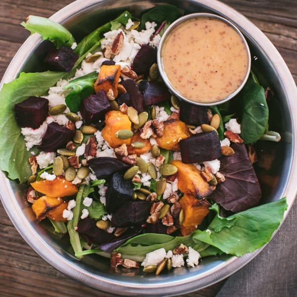 A vibrant salad with roasted beets, butternut squash, feta, pumpkin seeds, and pecans in a metal bowl.