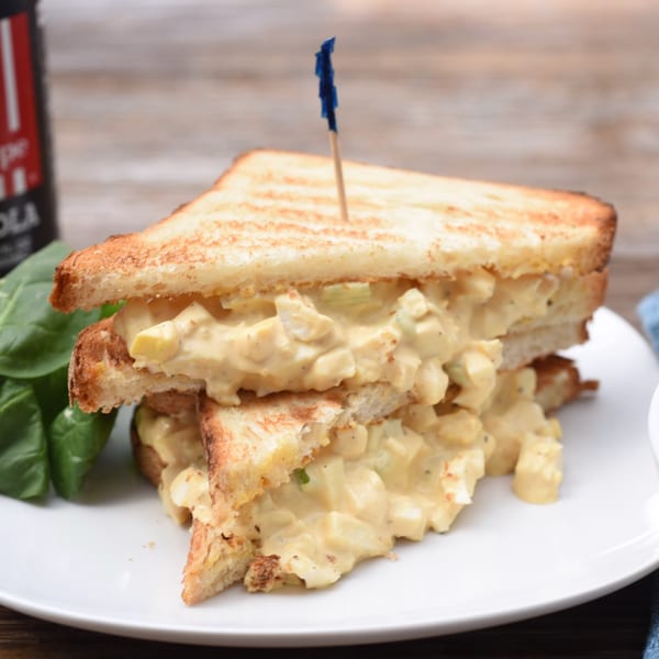 Toasted egg salad sandwich, cut in half and stacked, with a blue toothpick.